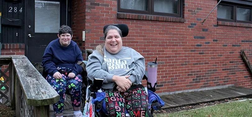 Woman in wheelchair smiling outside a brick building
